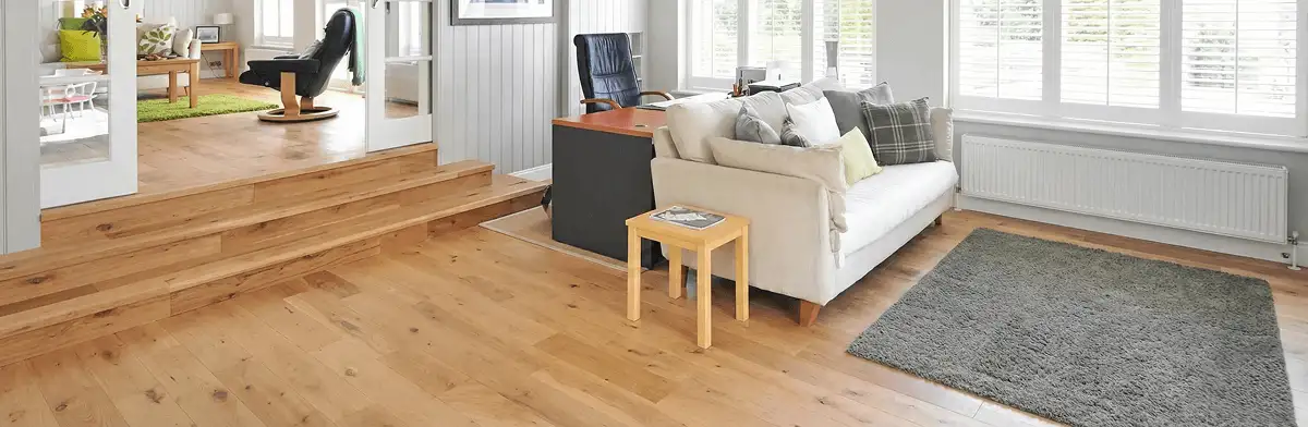 A modern living room with professionally installed laminate flooring, a beige sofa, a small side table, a gray rug, and large windows with white shutters in Sarasota, FL